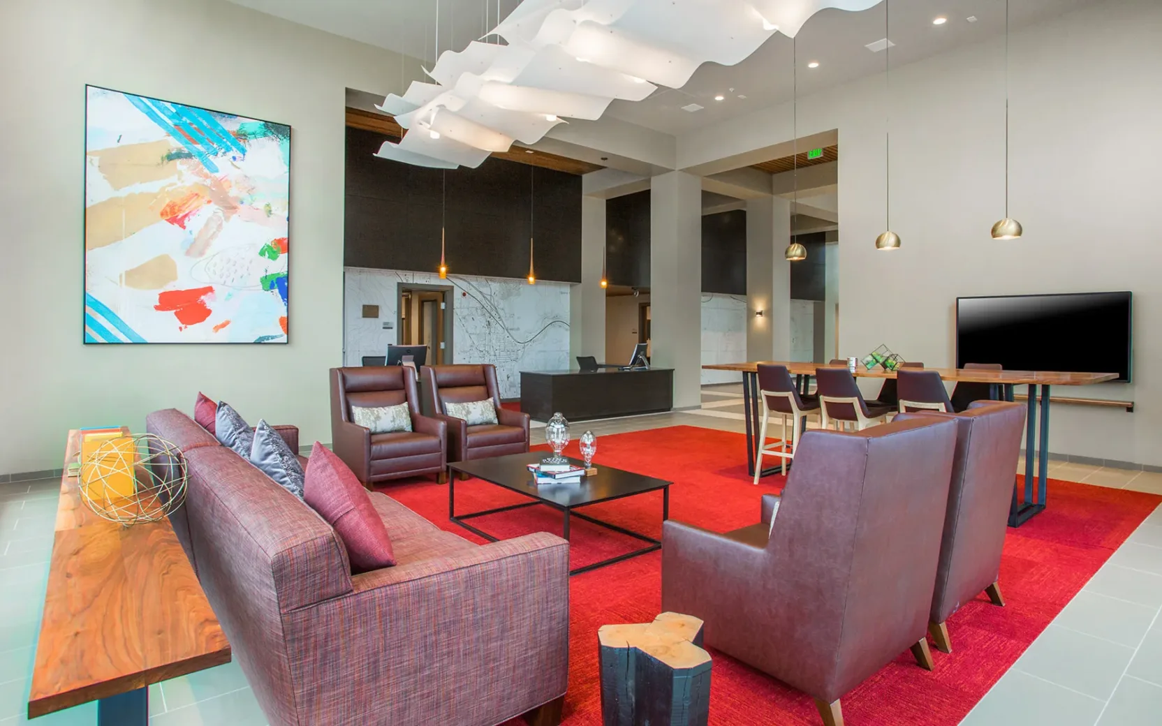 Modern apartment lobby with stylish furniture, featuring a red carpet, leather chairs, a wooden coffee table, and large abstract artwork on the wall.