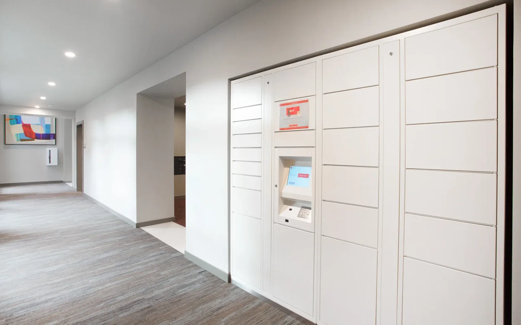 A hallway in an apartment building featuring a secure package locker system with multiple compartments and a digital screen for managing deliveries.