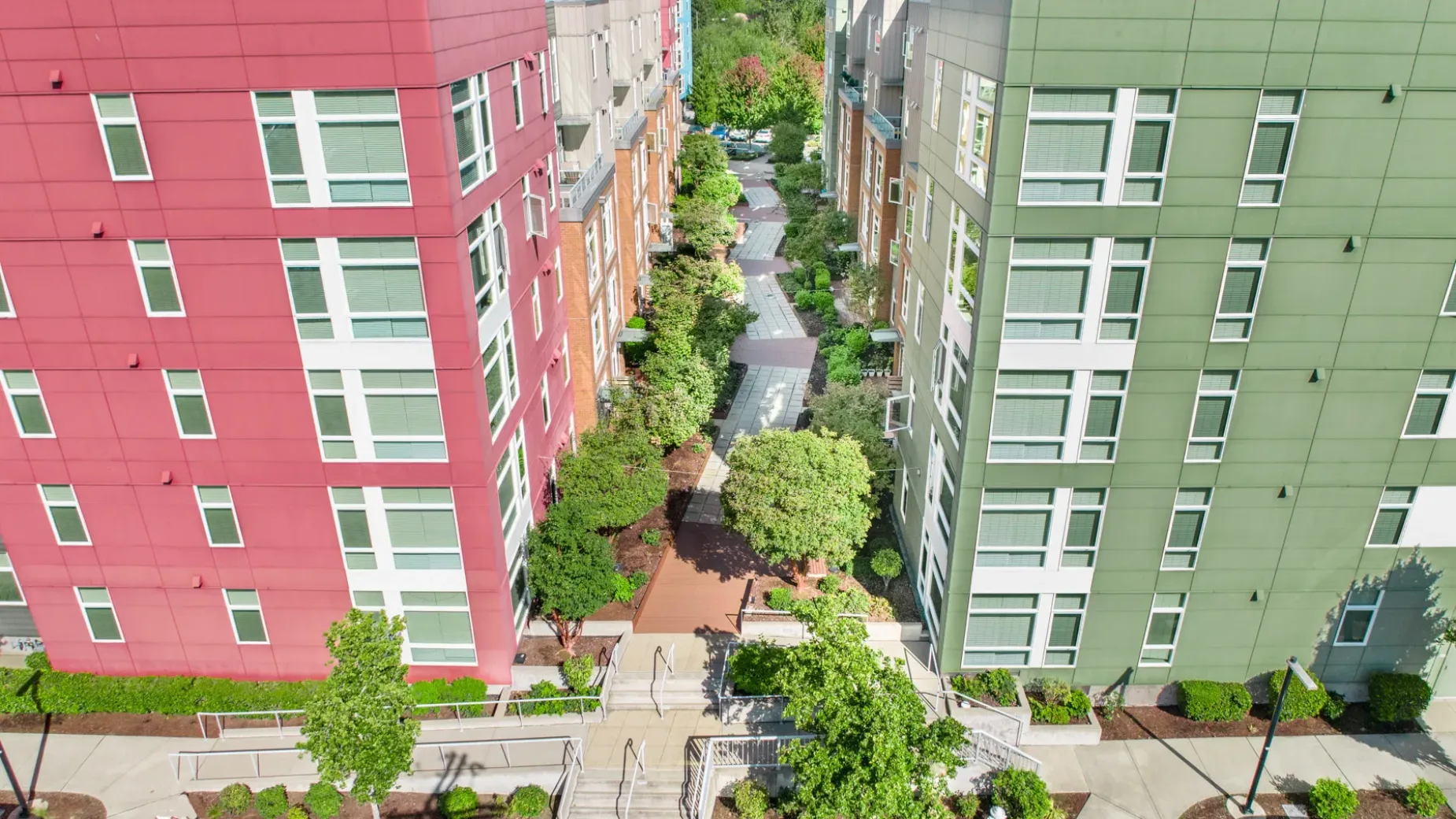Aerial view of two tall apartment buildings, one red and one green, with a landscaped pathway and trees between them.