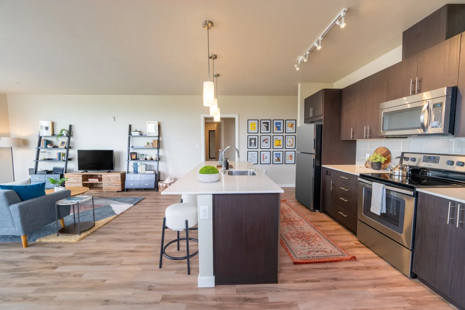 Modern apartment interior with an open-plan kitchen and living area, featuring wooden flooring, stainless steel appliances, and contemporary furniture.