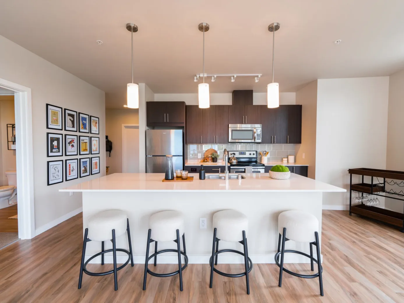 Modern apartment kitchen with a large island, stools, and stainless steel appliances.