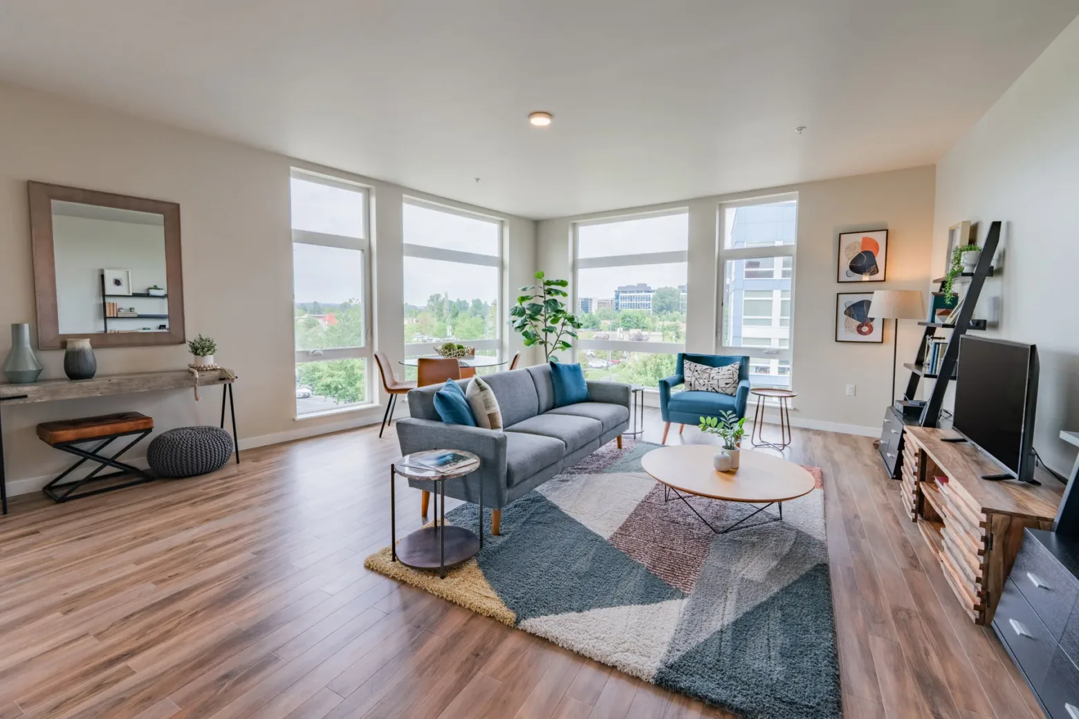Modern apartment living room with a gray sofa, colorful decor, and large windows offering a city view.